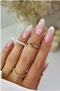 Elegant pink almond-shaped French tip nails with delicate white floral designs and gold rings.